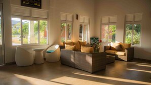 A spacious living room with a modern sofa set, a round coffee table, and a unique seating pod. Large windows allow natural light to fill the room. - Sungreen Resort (Habarana)