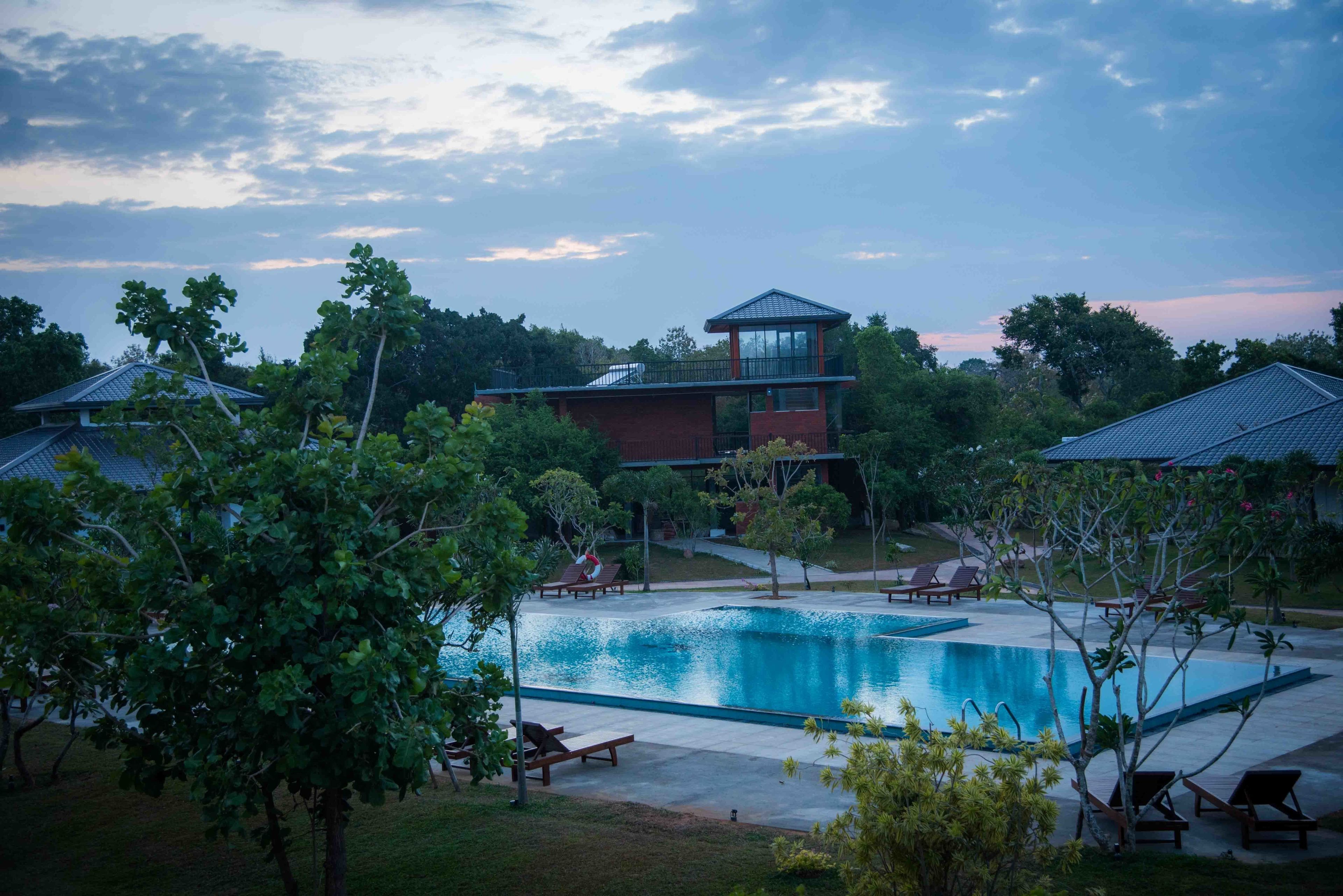 A swimming pool with lounge chairs and a building with a tower-like structure in the background.