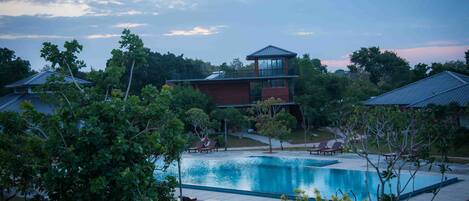 A swimming pool with lounge chairs and a building with a tower-like structure in the background.