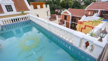 Una piscina con un diseño de sol en el suelo, rodeada por un balustrada blanca y un techo de tejas rojas.