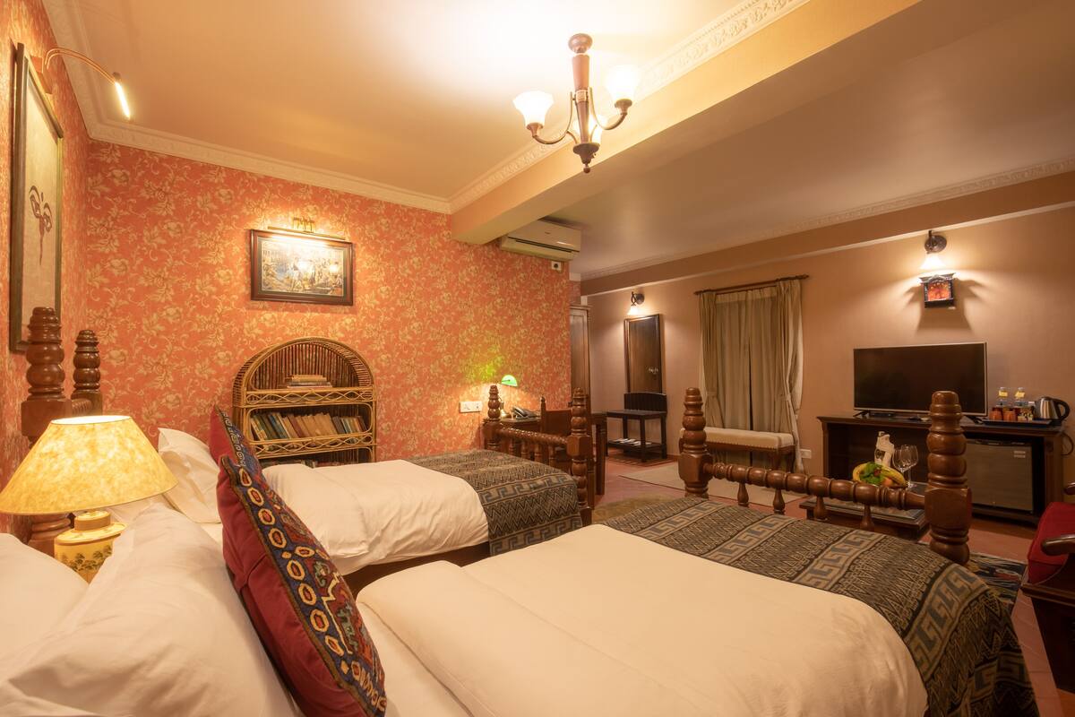 Habitación de hotel con dos camas, cabecero de madera, escritorio, silla, televisor y aire acondicionado de pared.