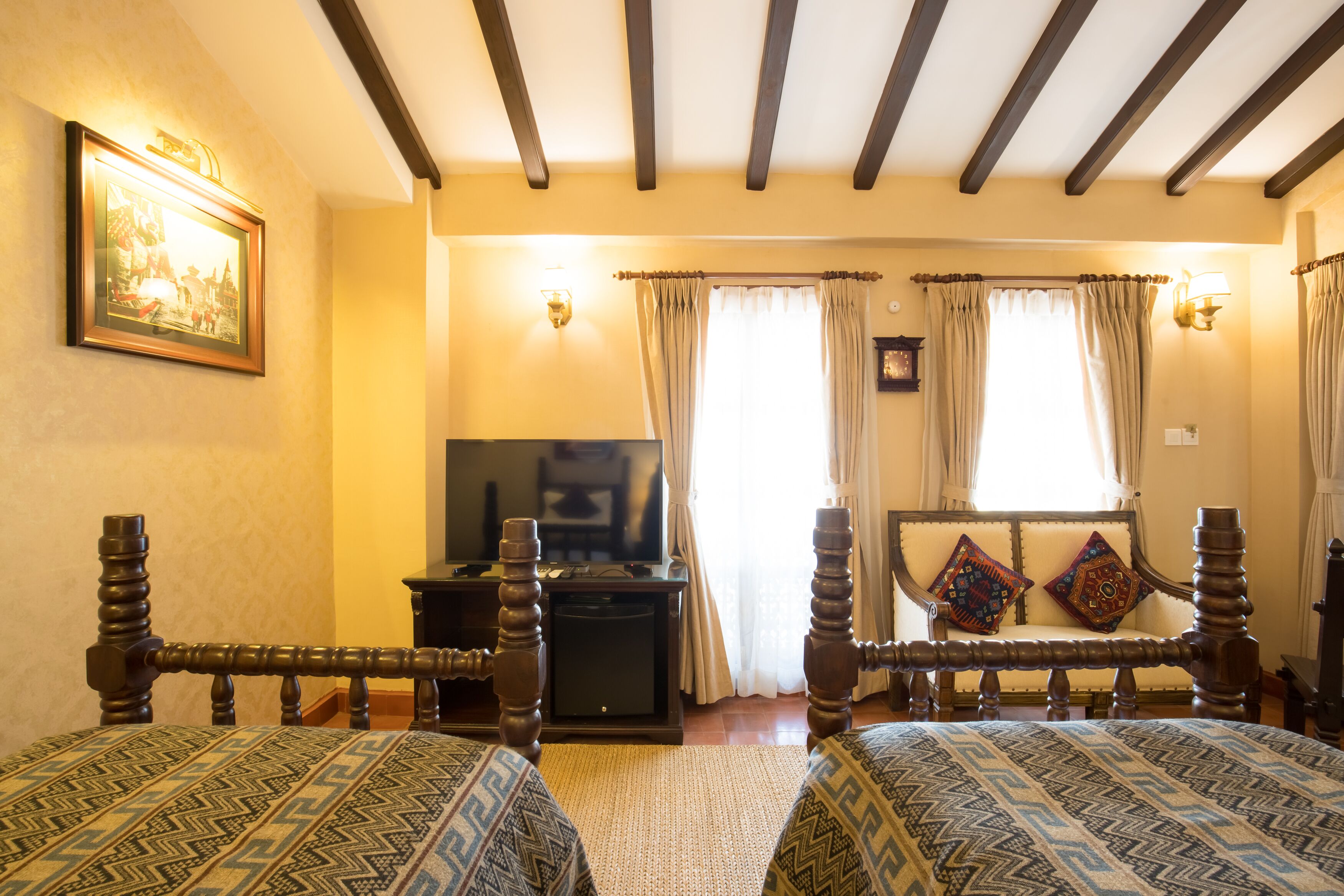 A room with two wooden beds with patterned bedding, a television on a stand, and a painting on the wall.