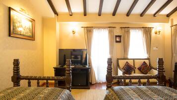 A room with two wooden beds with patterned bedding, a television on a stand, and a painting on the wall.