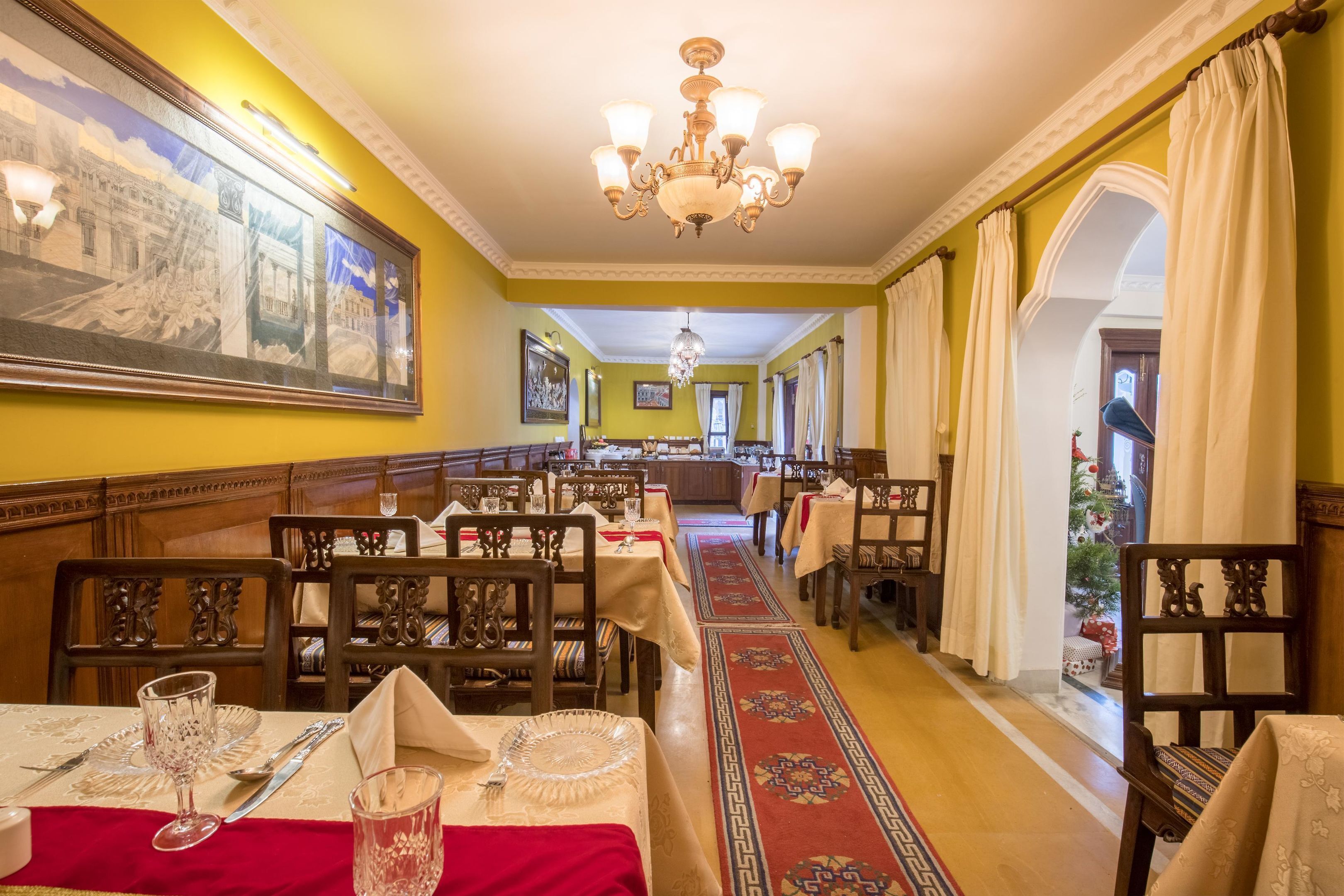A dining area with tables set for service, a chandelier, and a large painting on the wall.