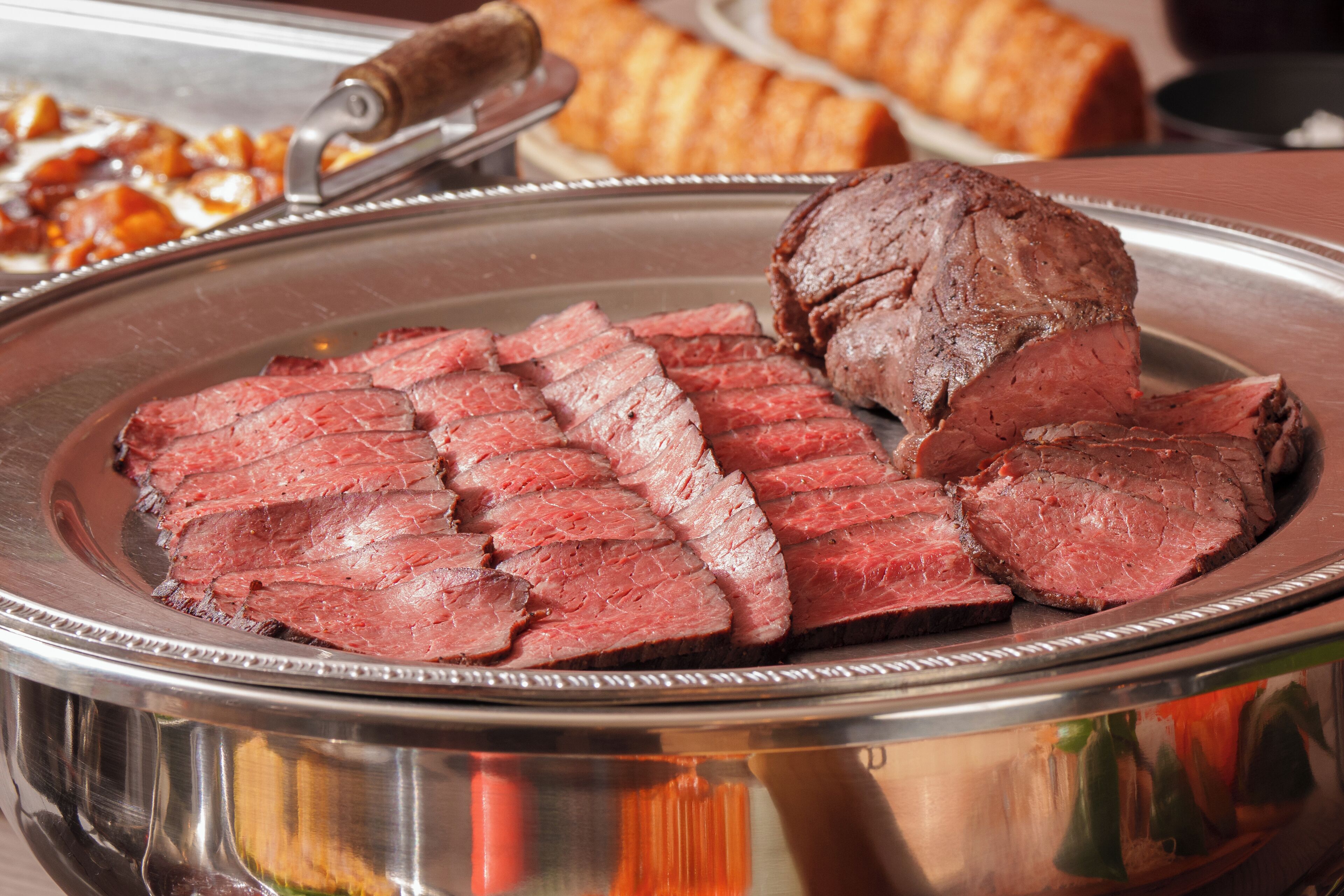 A metal serving dish with sliced beef and a whole beef roast.