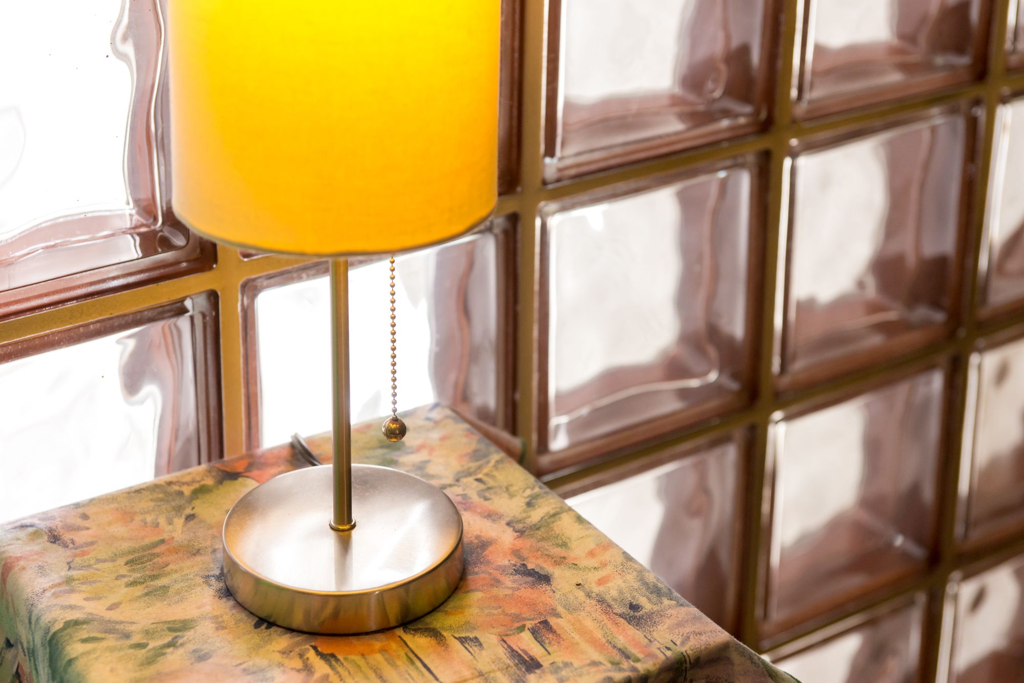 A table lamp with a yellow shade on a table with a textured surface.