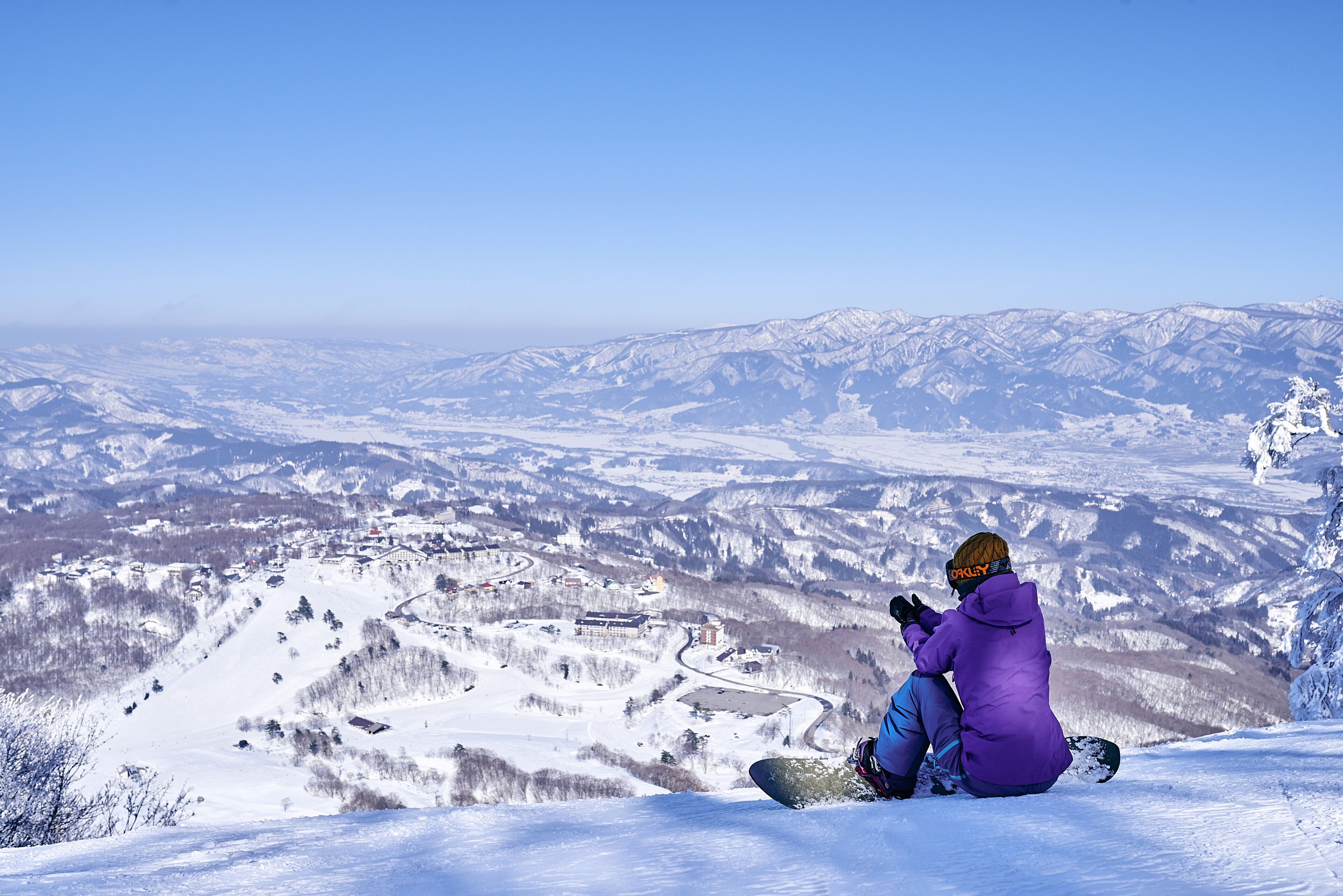 A person sitting on a snowy slope with a view of a snow-covered valley and mountains.