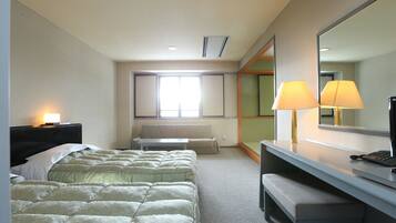 Habitación de hotel con cama, escritorio, silla, lámpara, espejo y ventana.