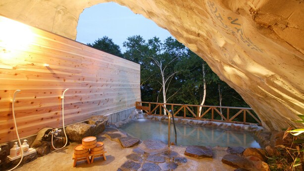 An indoor hot spring area with wooden walls, stone flooring, and a wooden deck overlooking the water. - Hotel Silk in Madarao (Iiyama)