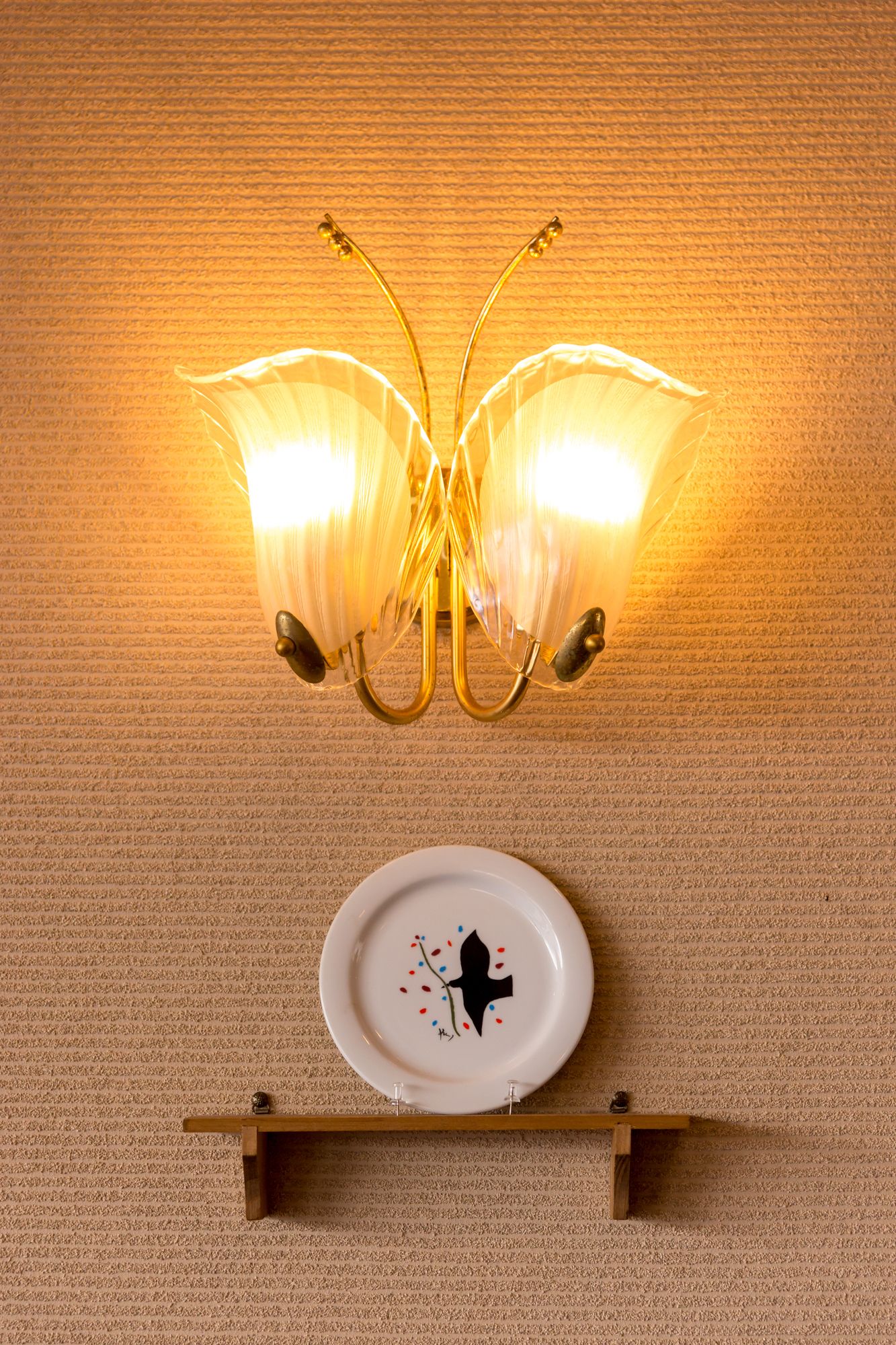 A wall-mounted chandelier with two lamps and a decorative plate below it.