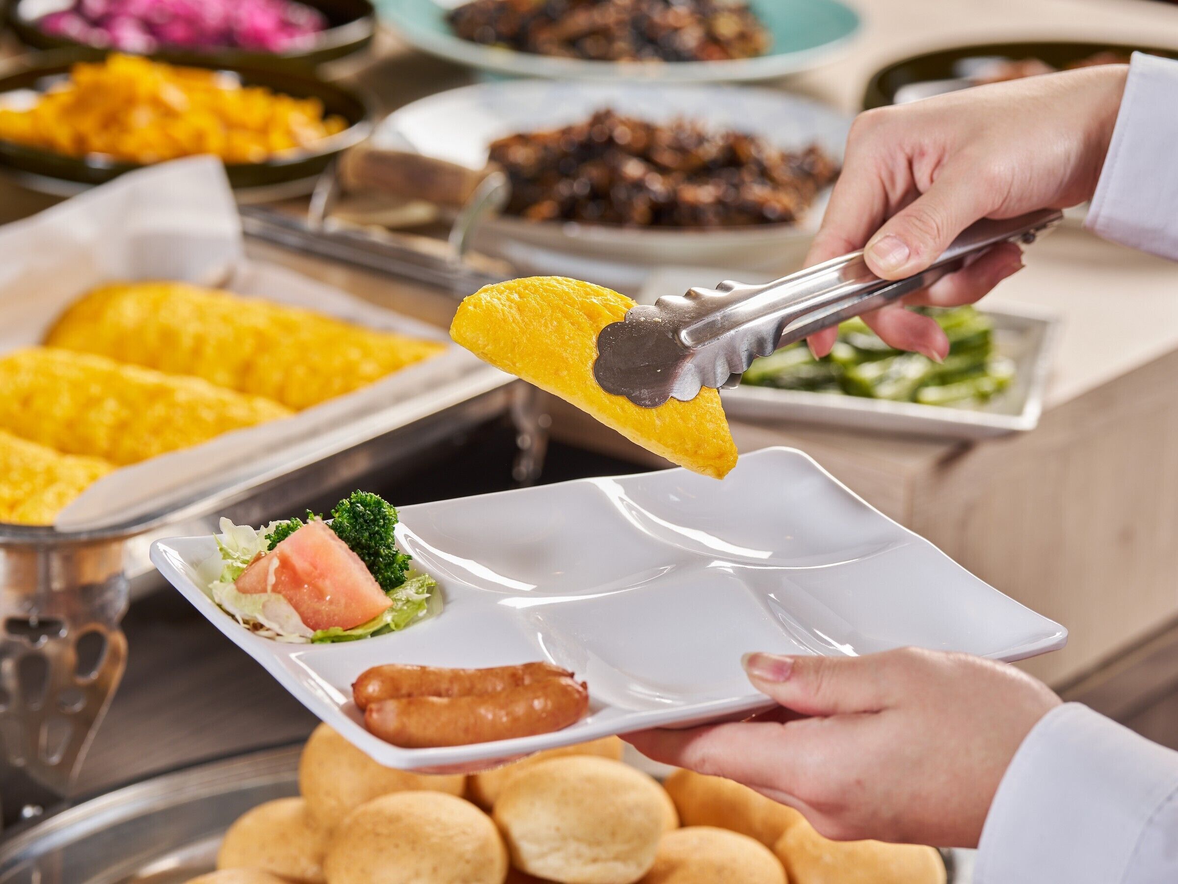 A buffet with various food items, including a plate with a piece of yellow food, a sausage, and a salad.