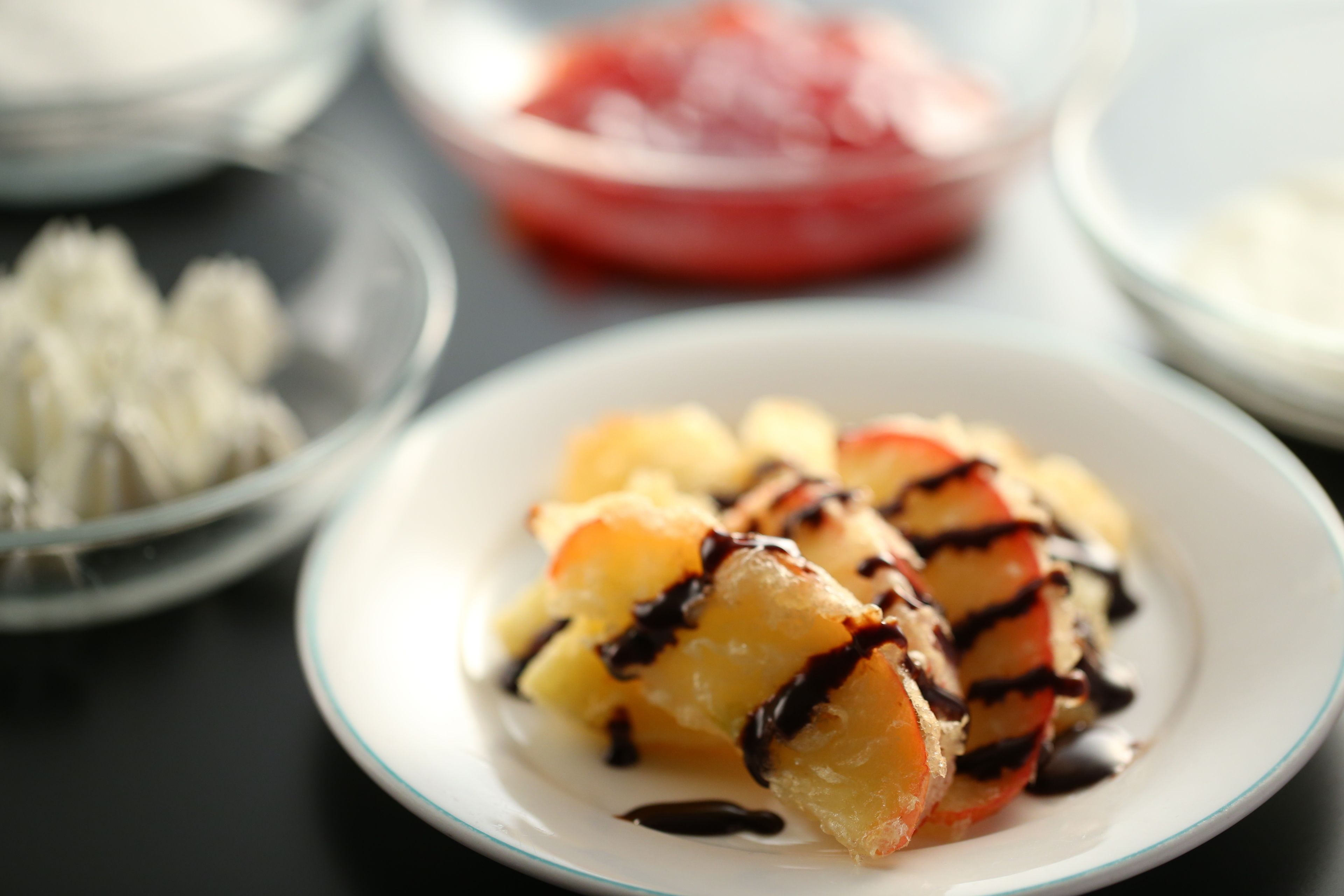 A plate of grilled fruit with chocolate drizzle, accompanied by a bowl of white sauce and a bowl of red sauce.