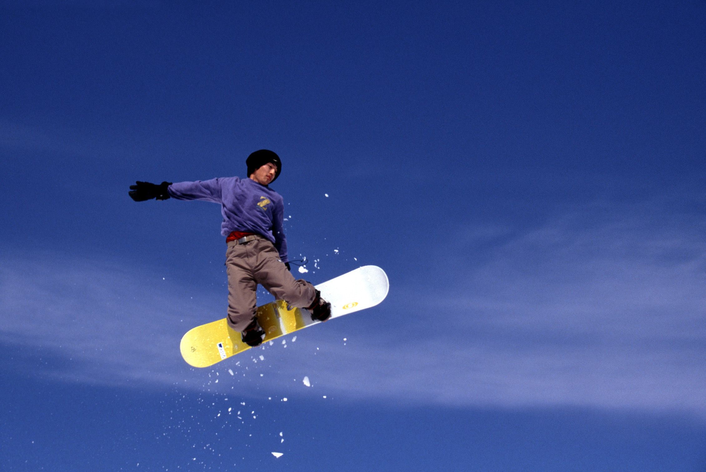 A snowboarder in mid-air against a clear blue sky.