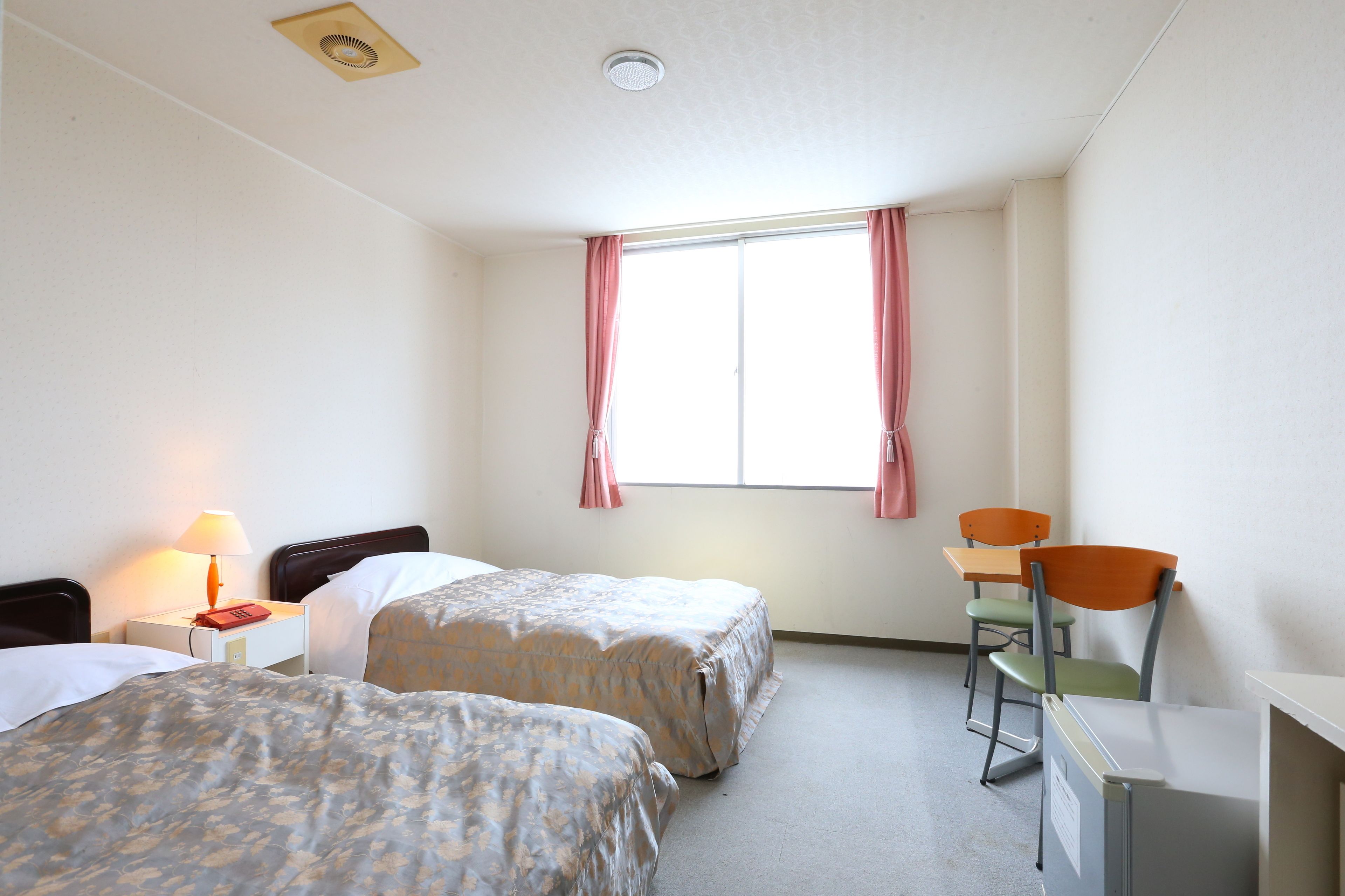 Habitación de hotel con dos camas, un escritorio, una silla, una lámpara y una ventana con cortinas.