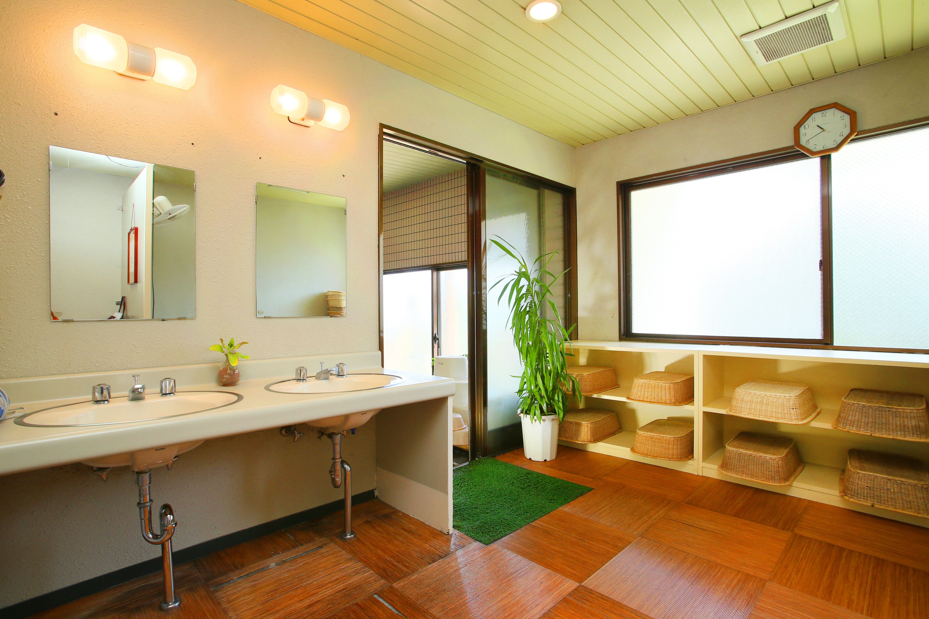 Un baño con dos lavamanos, un espejo, un reloj y una planta en maceta.