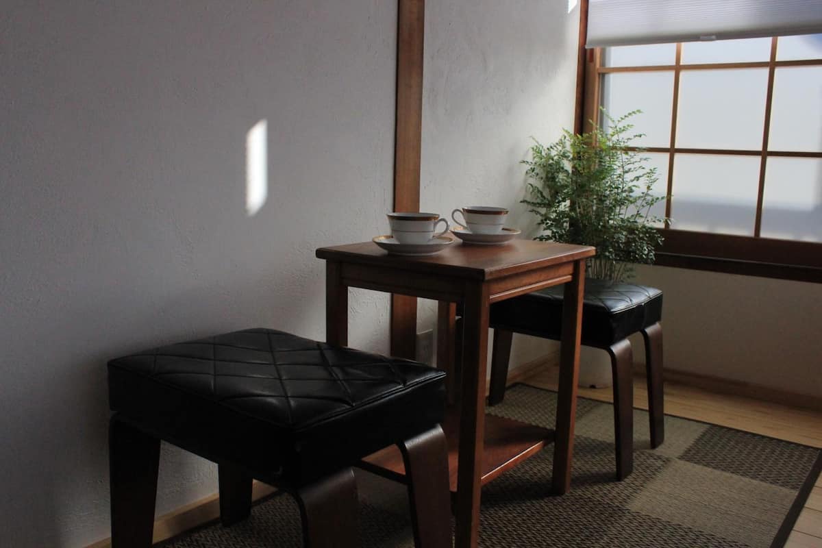 A small room with a wooden table, two black stools, and a potted plant near a window.