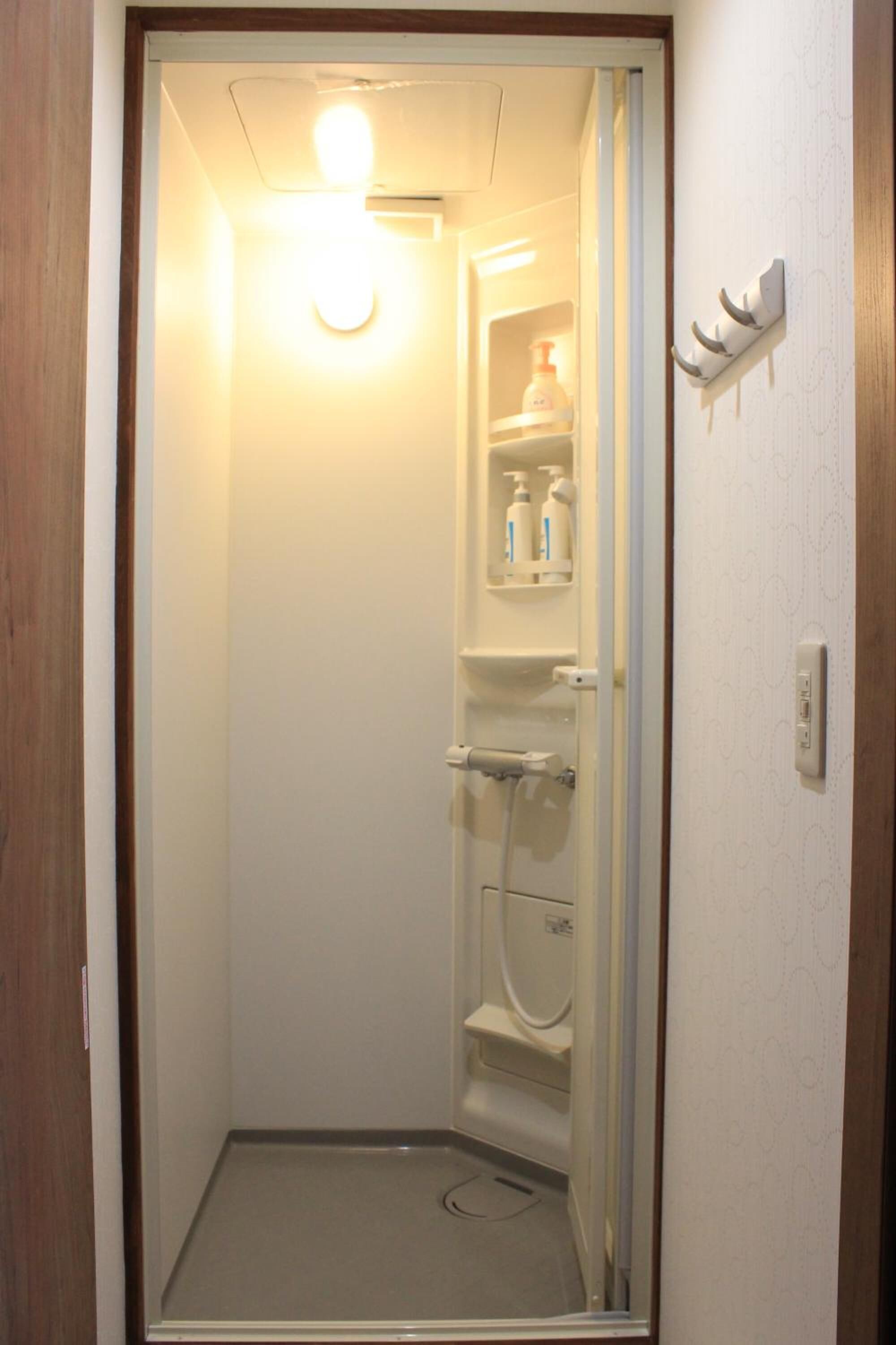 A small, enclosed bathroom with a toilet, a shower, and a shelf with toiletries.