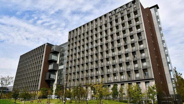 A modern building with a grid of windows and balconies, surrounded by a green lawn and trees. - Hostel HANA AN (Tokyo)