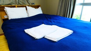 A neatly made bed with a blue bedspread and white pillows, a wooden headboard, and a bedside table with a lamp. - Hostel HANA AN (Tokyo)