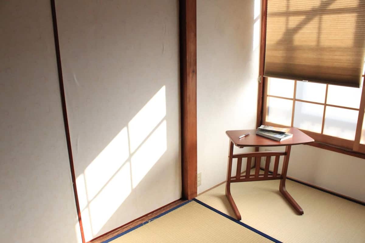 A traditional Japanese room with tatami flooring, a shoji screen, and a small wooden table with a book.