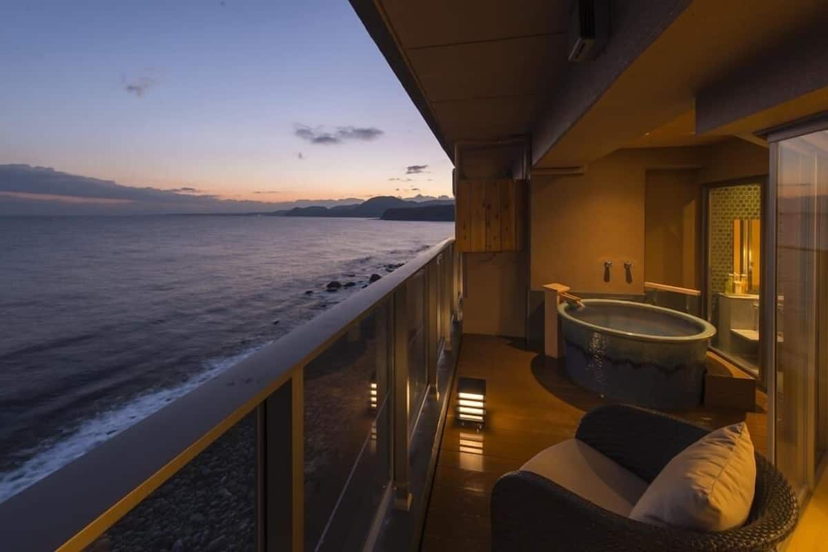 A balcony with a view of the sea, a hot tub, and a seating area.