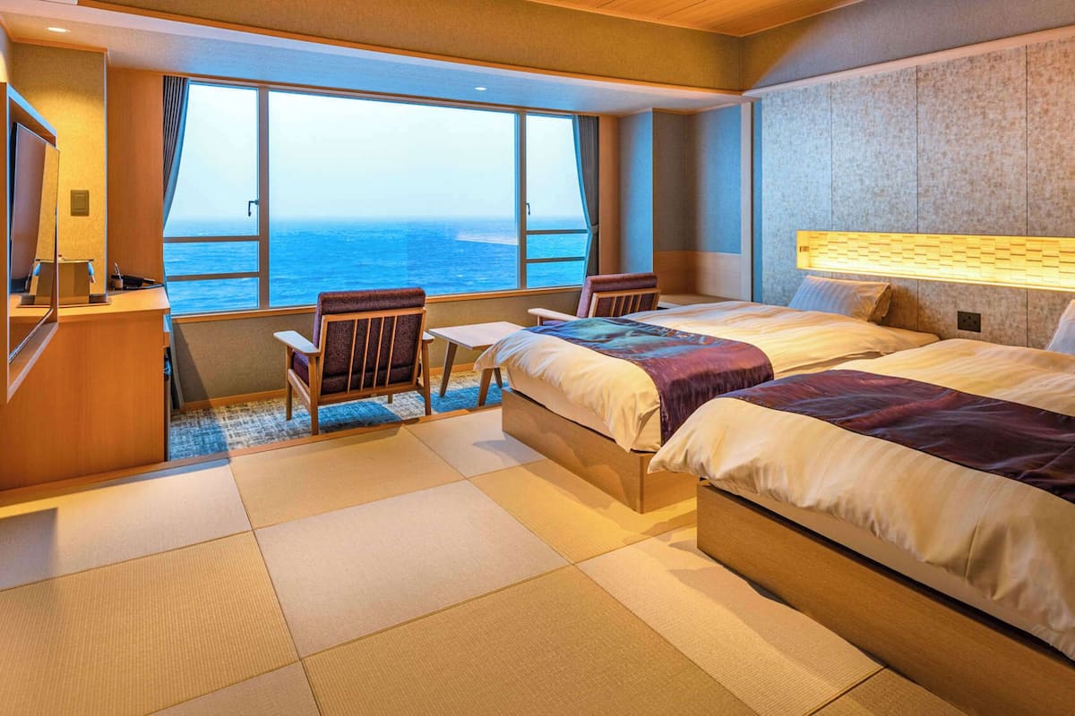 A hotel room with a large window, a bed, a desk, and a chair.