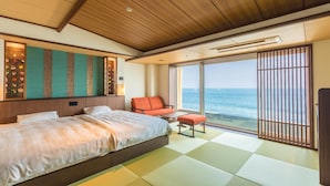 A hotel room with a large bed, a seating area with a view of the sea, and a sliding door to the outside. - Inatoriso (Higashiizu)