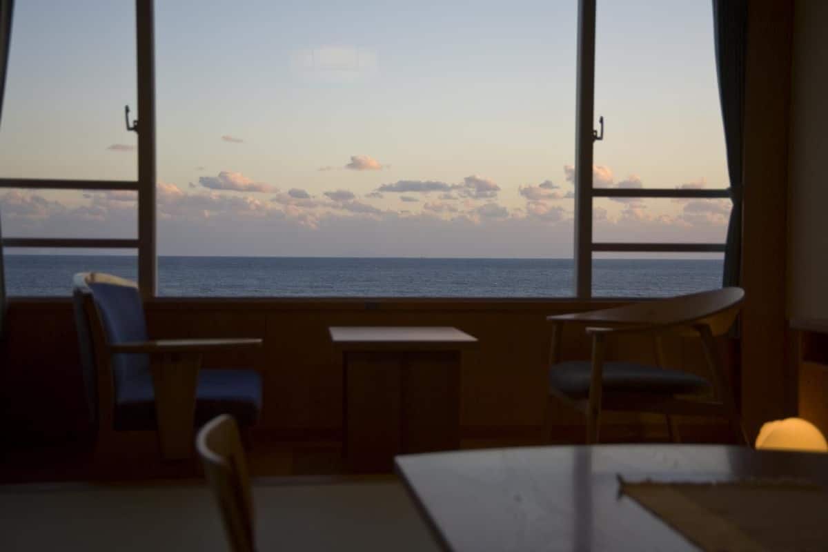 A room with a view of the sea through large windows, a small table, and two chairs.