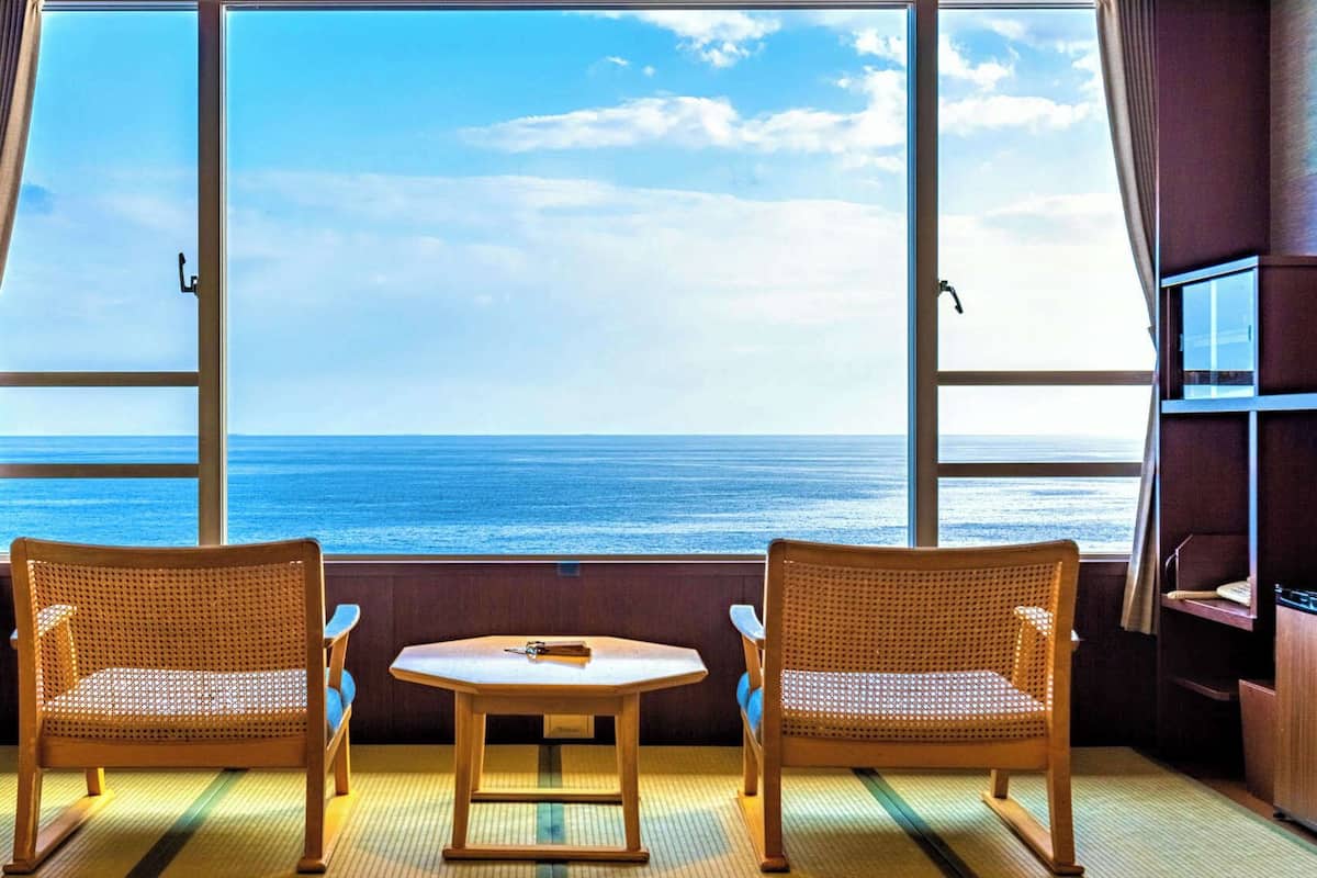 A room with two wicker chairs, a small table, and a view of the ocean through large windows.