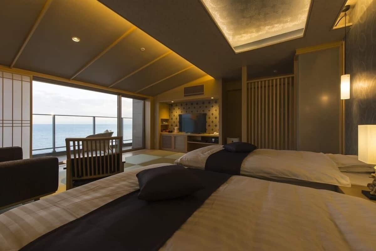 A modern hotel room with two beds, a TV, and a balcony with a view of the sea.