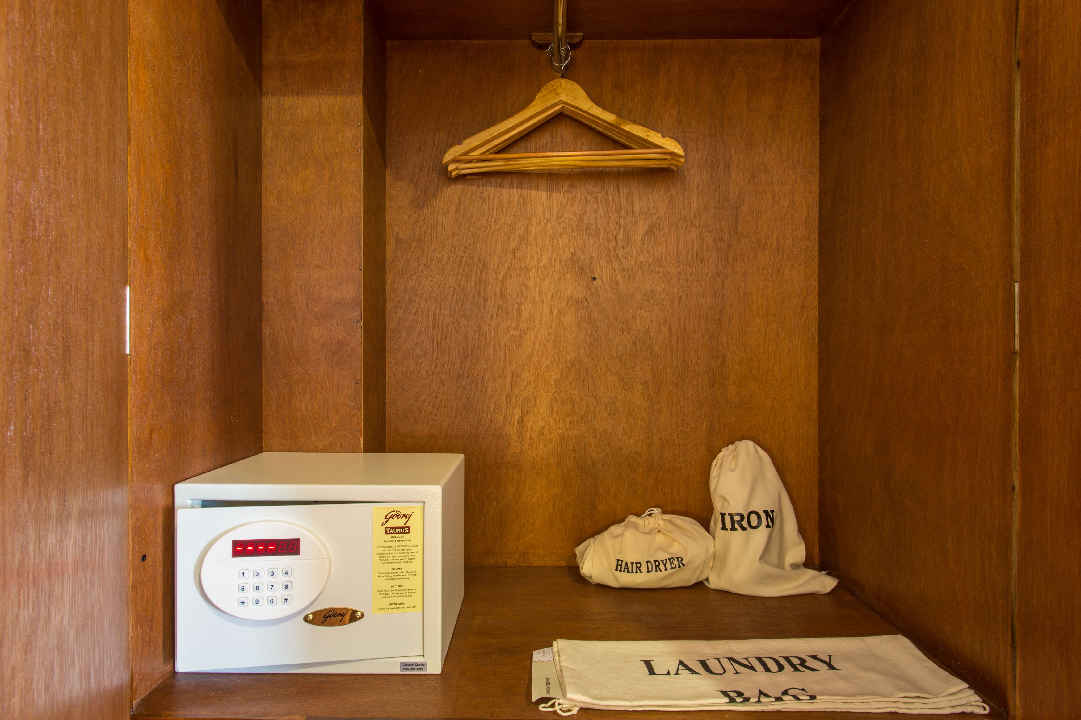 A compact room with a wooden wardrobe, a hair dryer, and a laundry bag.