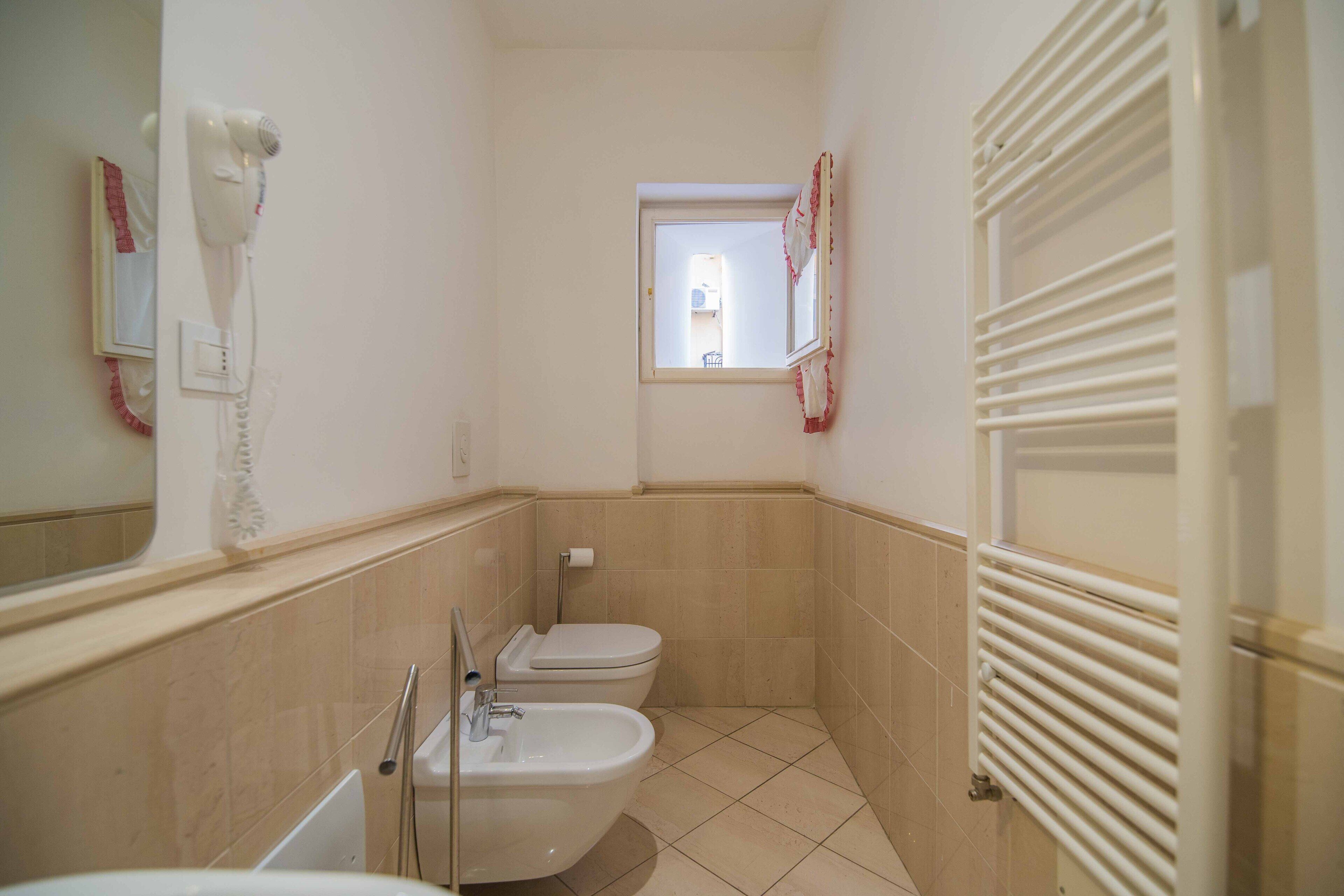 Een kleine badkamer met toilet, bidet en een haardroger bevestigd aan de muur.