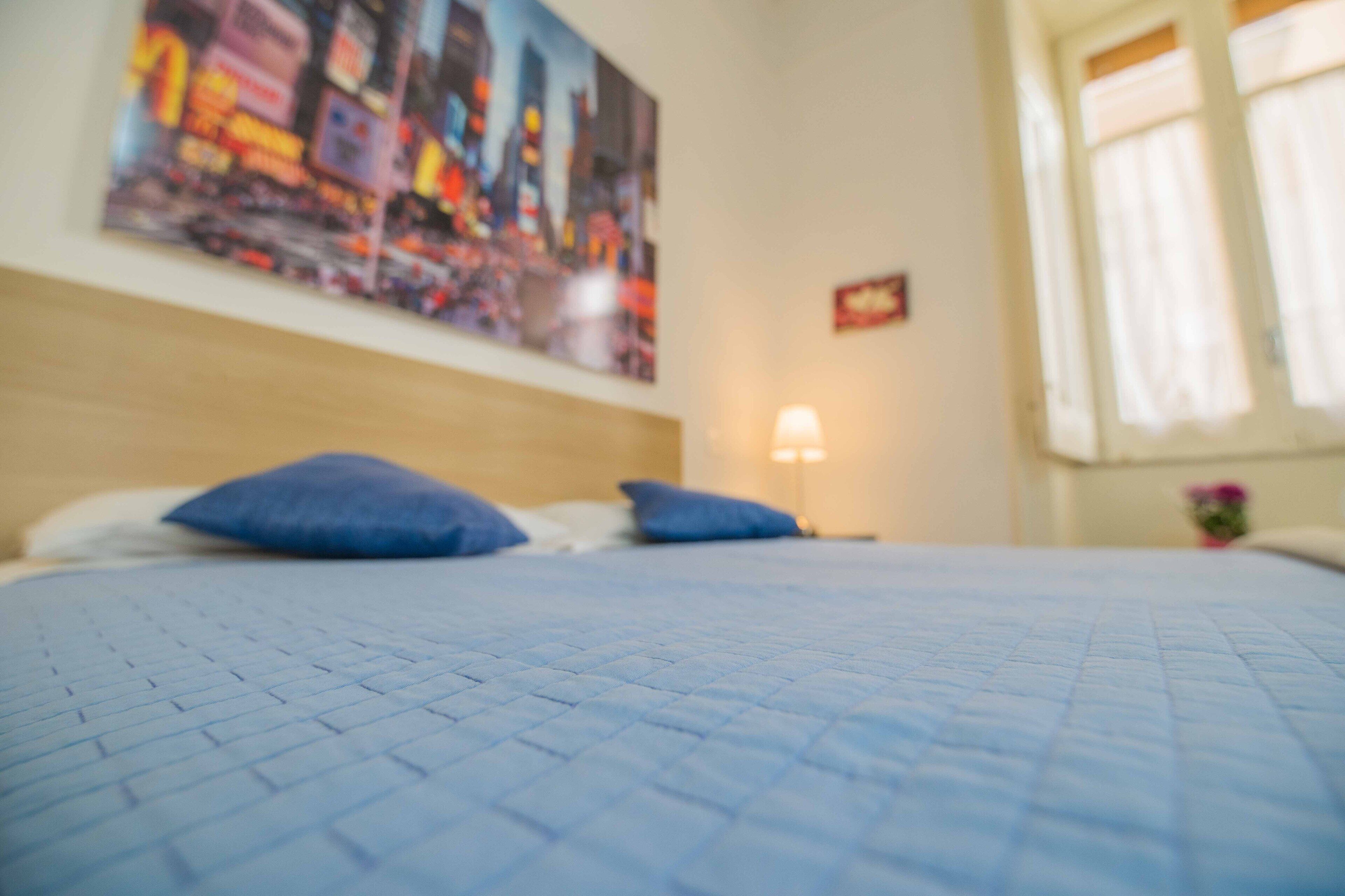Een bed met een geborduurde blauwe deken, een hoofdbord en twee kussens.