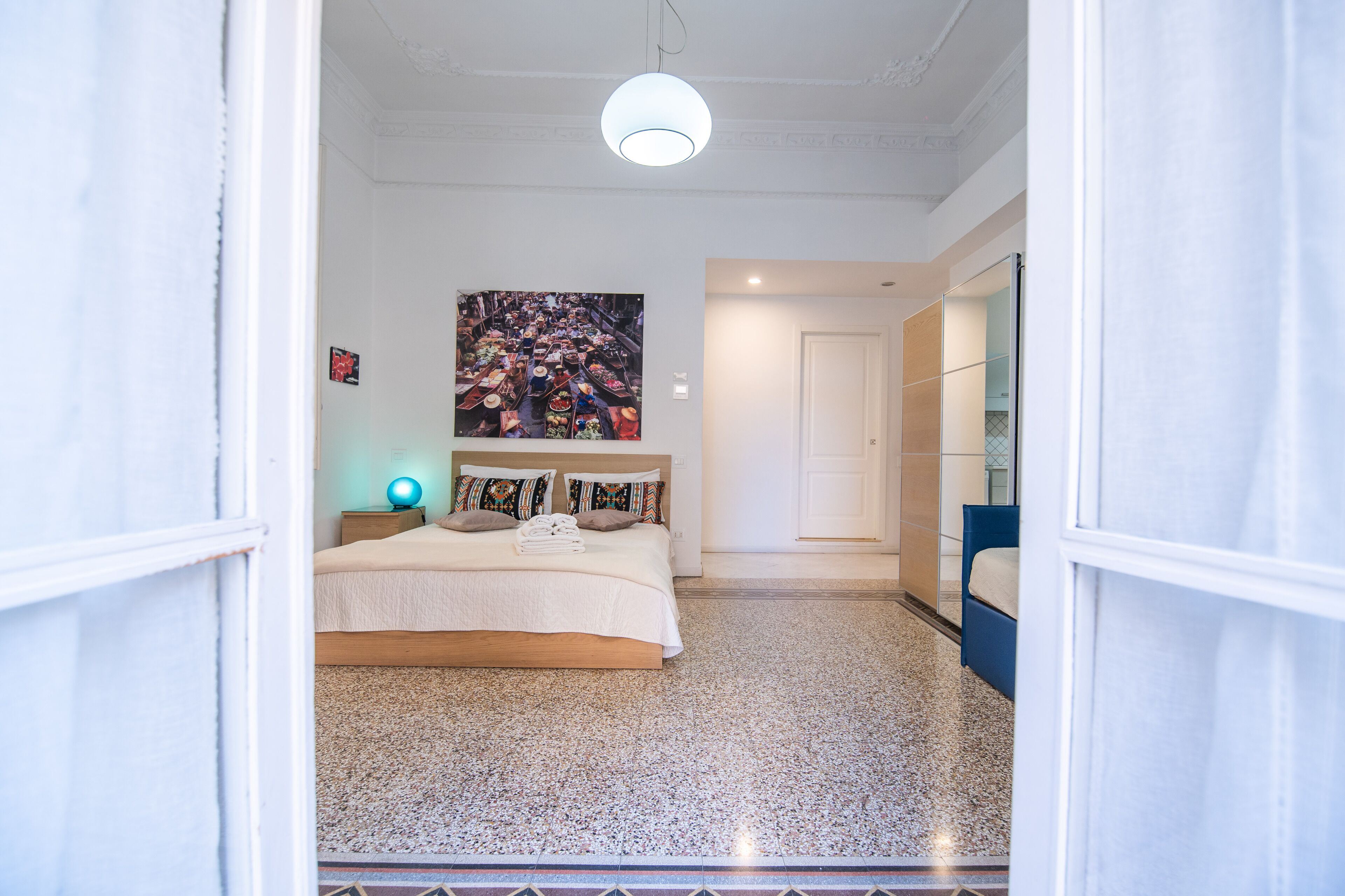 A bedroom with a bed, a bedside table, a wall-mounted artwork, and a door leading to another room.