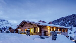 A wooden lodge with a stone entrance, surrounded by snow-covered mountains. - Severins The Alpine Retreat (Lech am Arlberg)