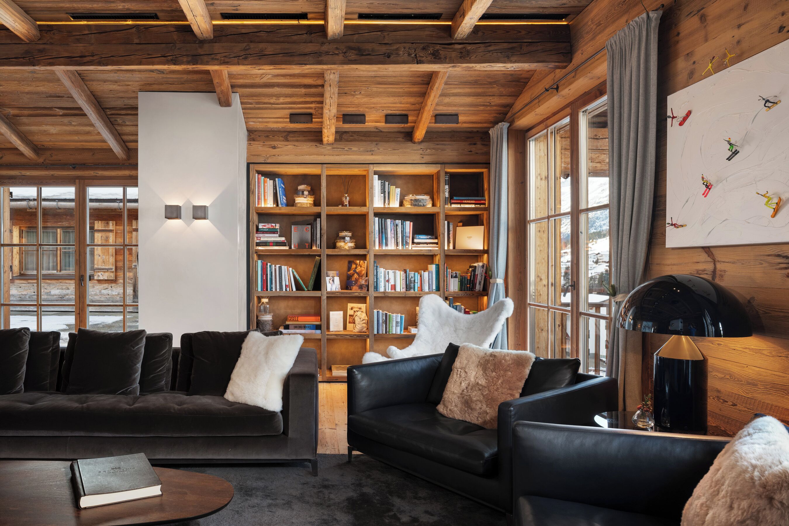 A cozy living room with a fireplace, a bookshelf, and a large window with a view of the outside.