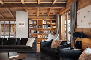 A cozy living room with a fireplace, a bookshelf, and a large window with a view of the outside. - Severins The Alpine Retreat (Lech am Arlberg)