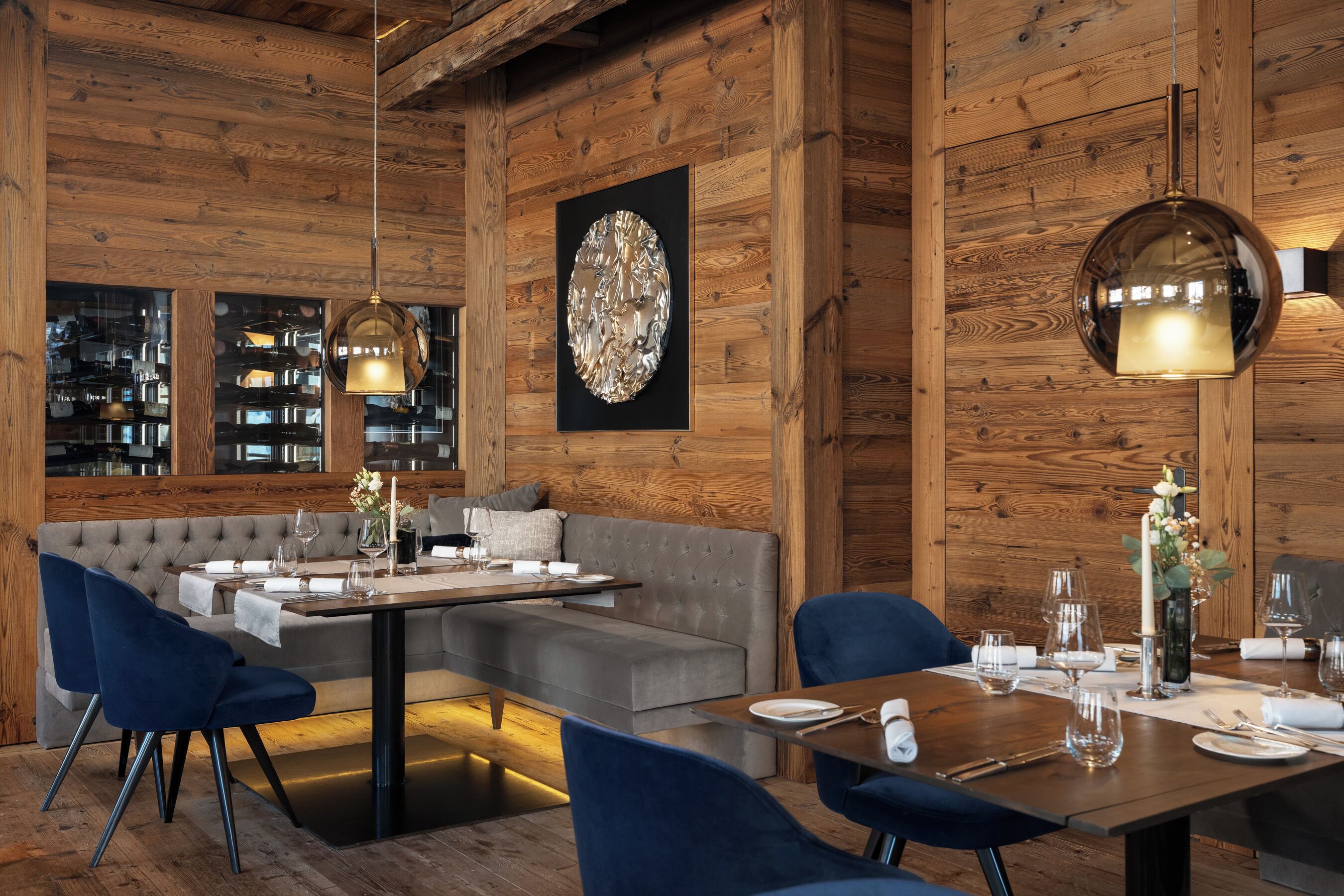 Un interior moderno con pared de madera, un sofá modular, una mesa de comedor lista para dos personas e iluminación colgante.