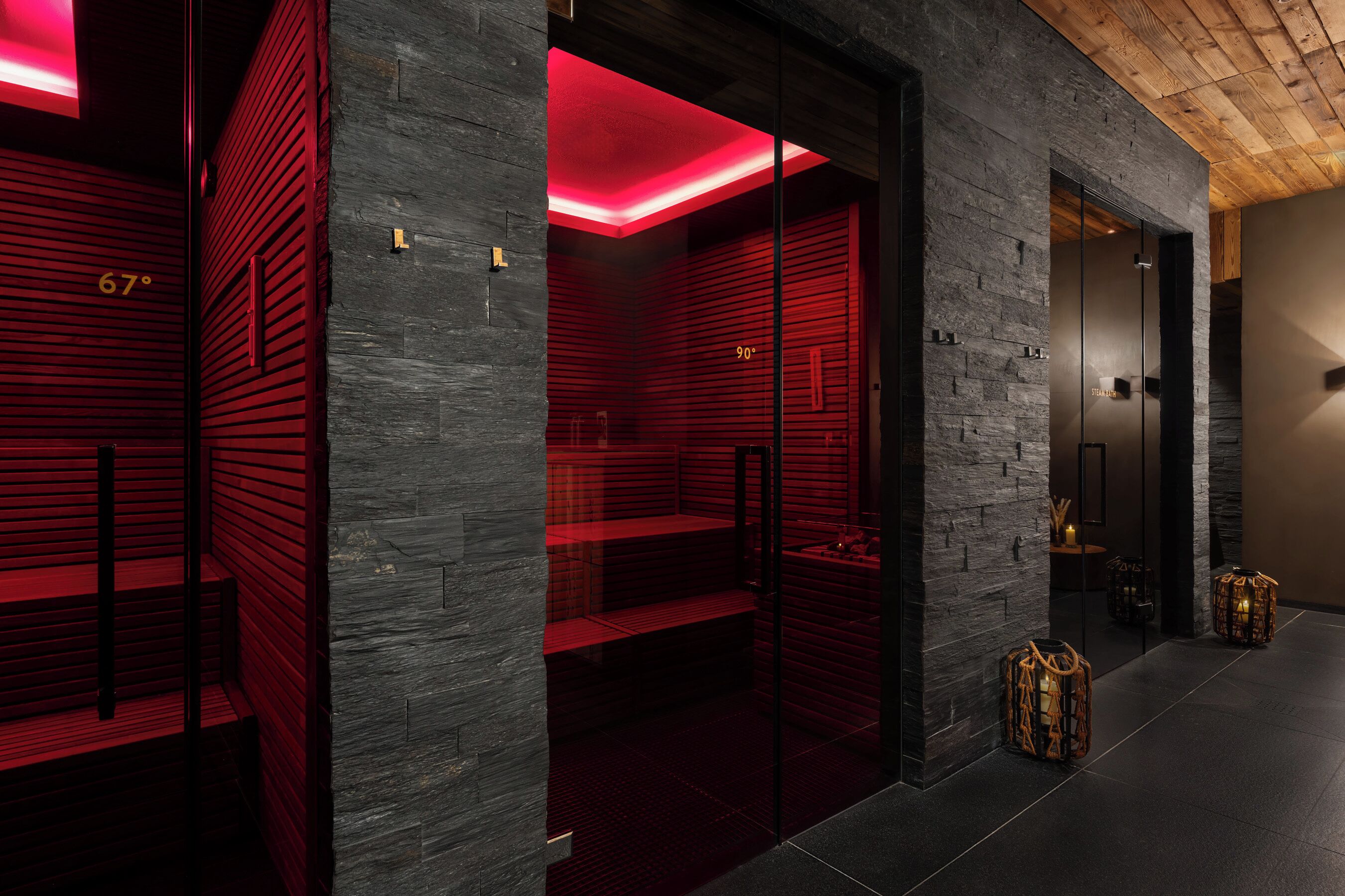 Ein modernes Interieur mit Steinwand, roter Beleuchtung, einem Bereich für ein Dampfbad und einer Holzbalkendecke.