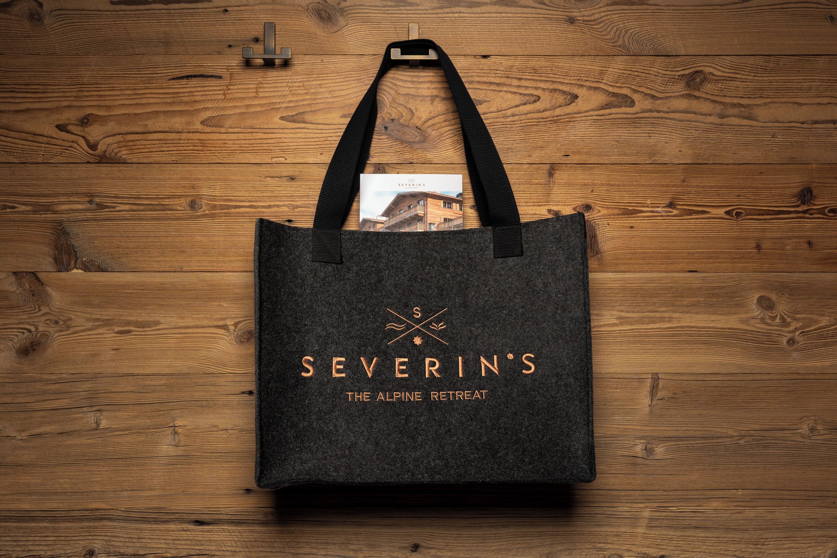 A dark tote bag with the text 'SEVERIN'S THE ALPINE RETREAT' and a logo, placed on a wooden floor.
