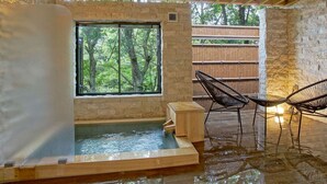 A spa area with a hot tub, wooden seating, and a view of trees through a window. - Mori No Izumi (Ito)