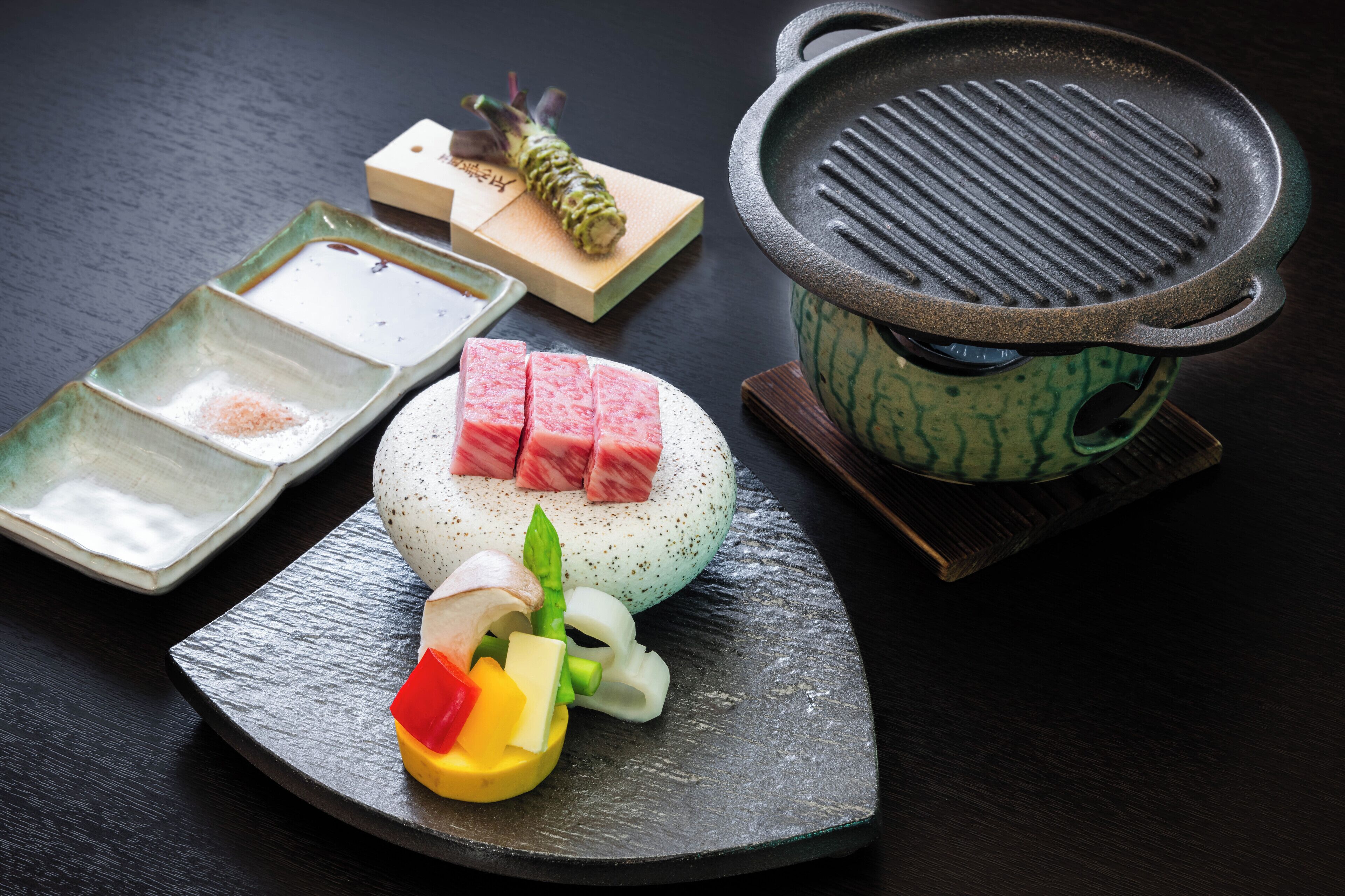 A table with a hot pot, a plate with sliced meat, vegetables, and a small dish with soy sauce.
