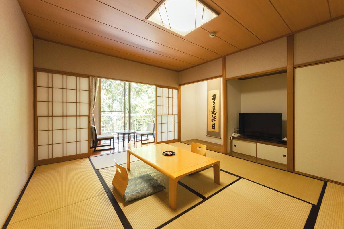 A traditional Japanese room with tatami flooring, a low table, chairs, a television, and sliding doors.