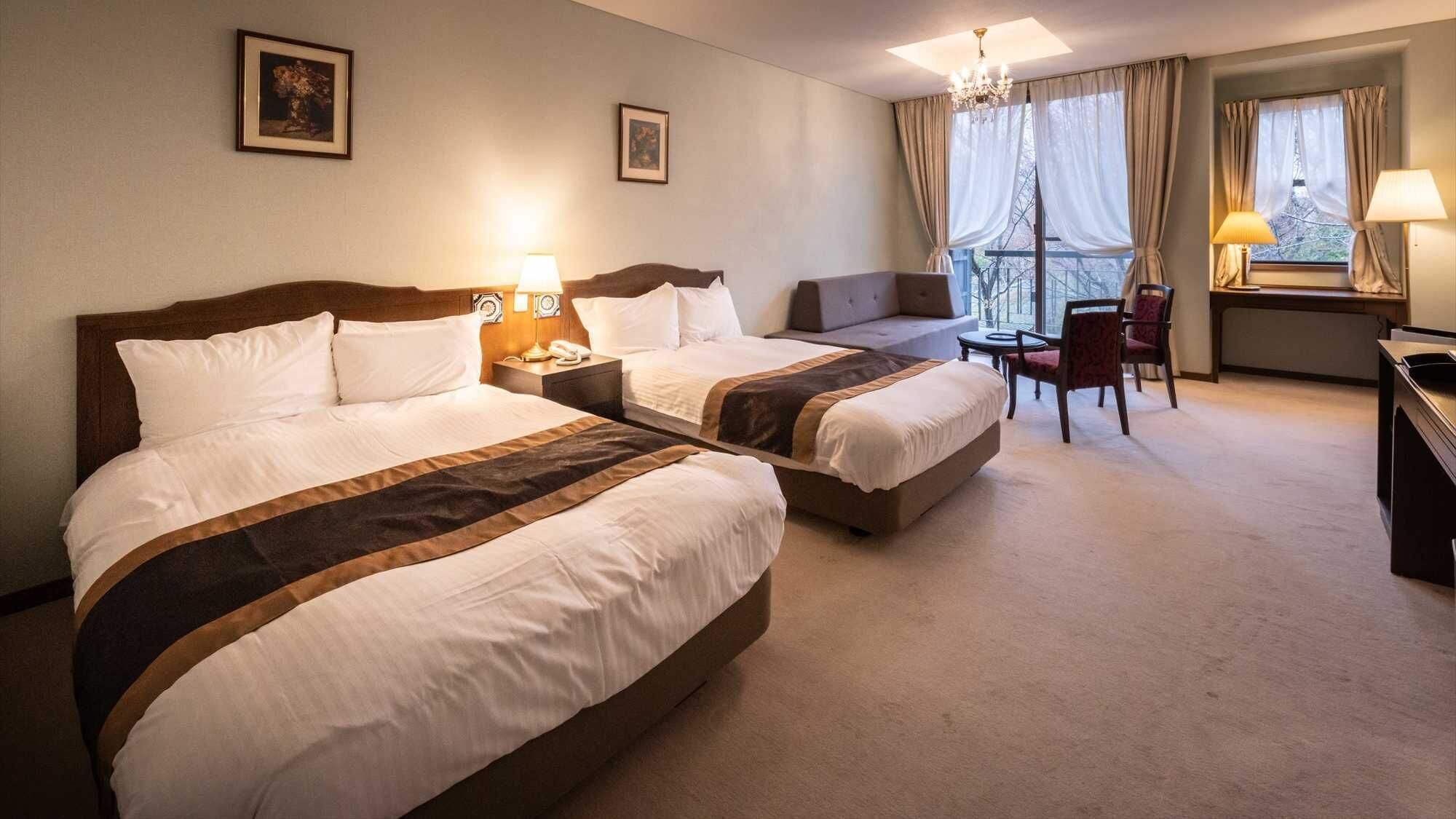 A hotel room with two beds, a desk, a chair, and a view of the outdoors.