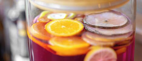 A glass container with a wooden lid filled with a red liquid and slices of orange and lemon.