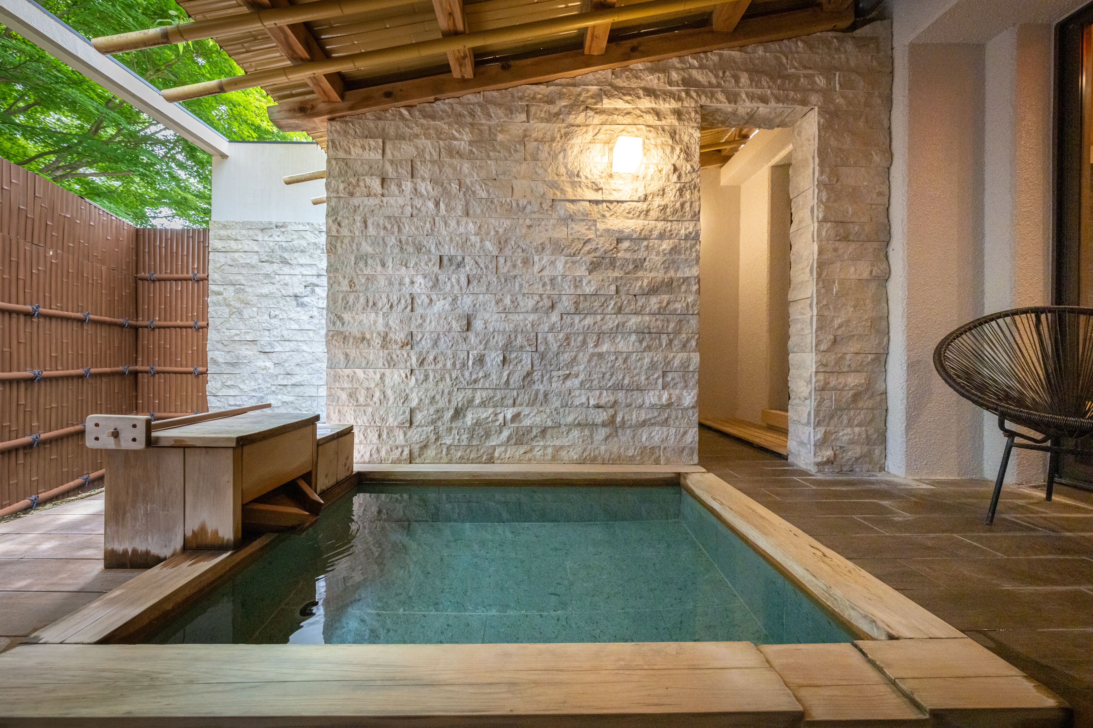 Zona de piscina interior con paredes de piedra, un banco de madera y una silla.