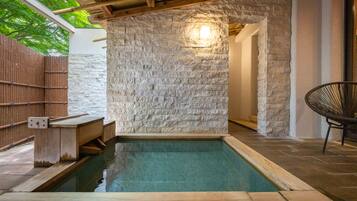 Zona de piscina interior con paredes de piedra, un banco de madera y una silla.
