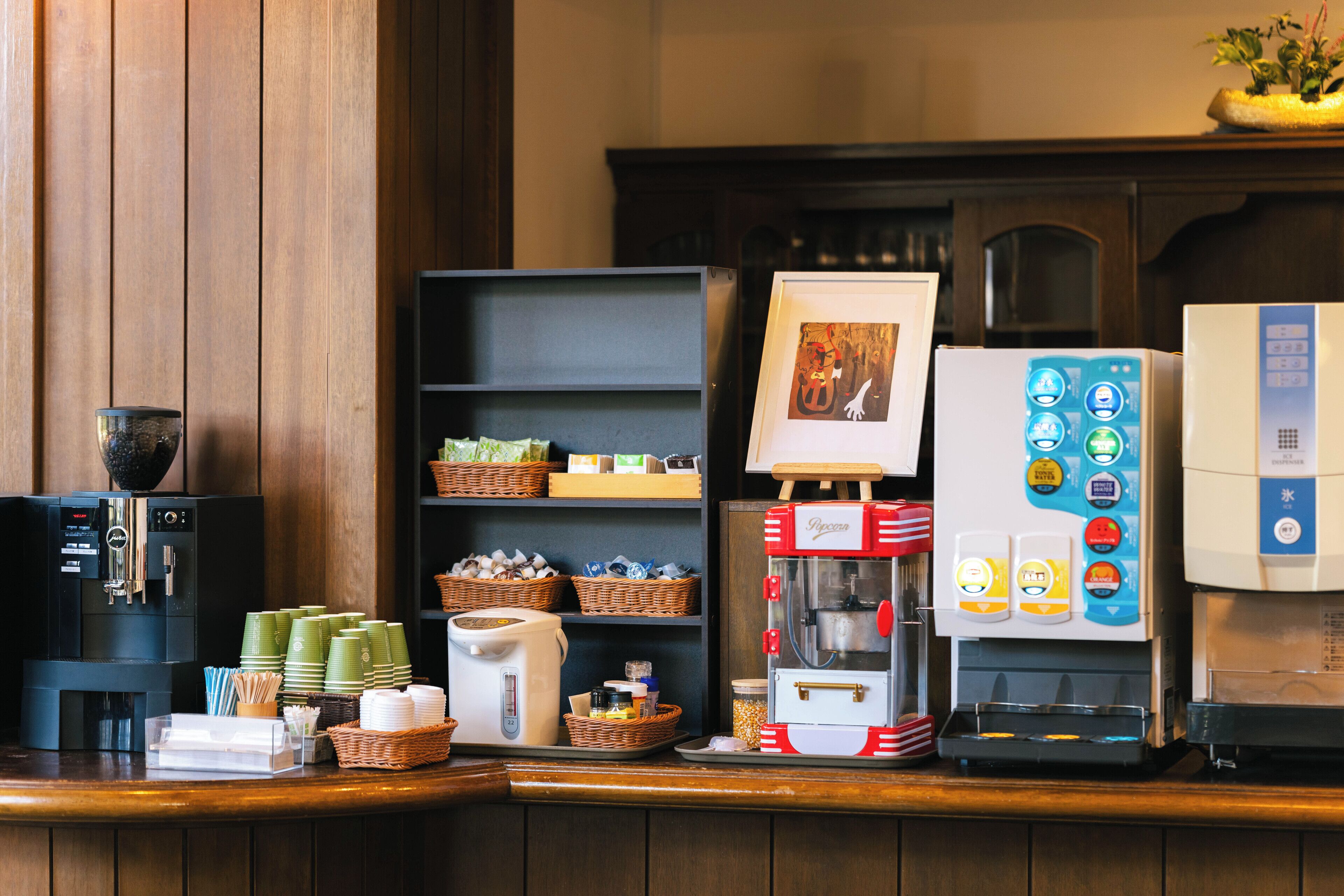 A coffee station with a coffee machine, a milk frother, and a display of coffee cups and a coffee grinder.