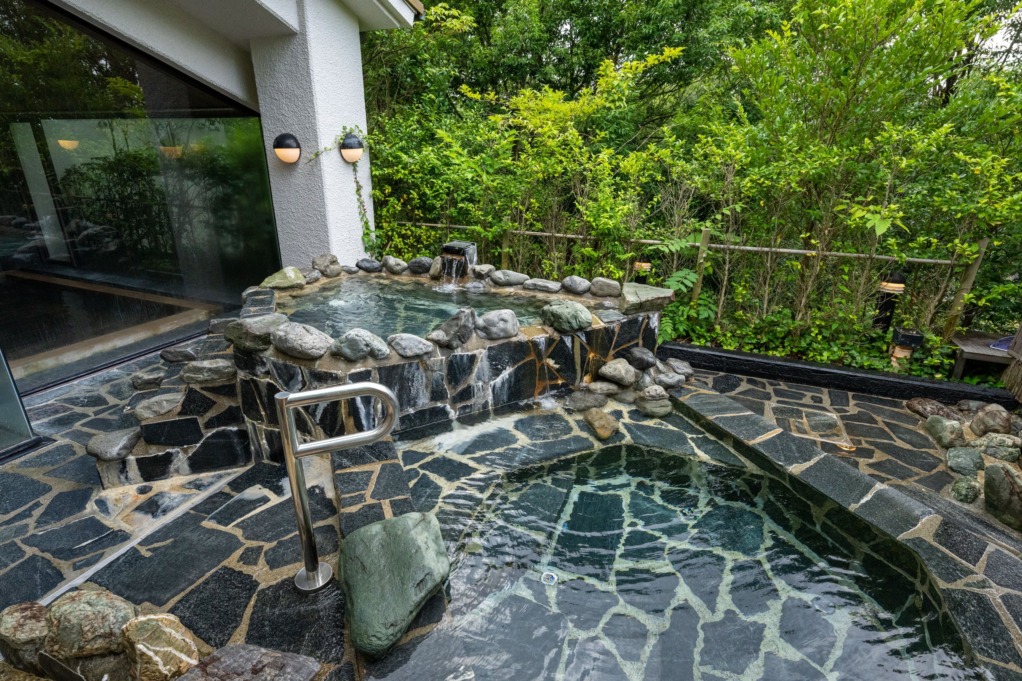 A hot spring area with a stone pool and a small waterfall, surrounded by greenery.