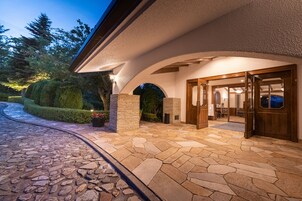 A stone-paved entrance with a wooden door, a stone wall, and a well-lit interior visible through the doorway.